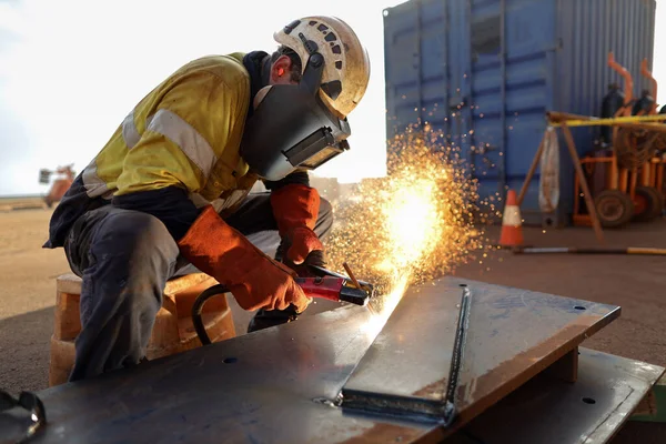Safety work place construction worker wearing safety ears plug  helmet, face shield, red welding leather glove protection while commencing hot work gouging metal plate repairing on the ground surface construction mine site  