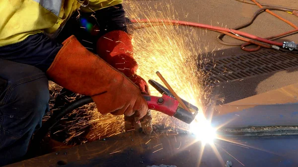 Safety work place macro pic of construction miner wearing a red welding lather glove protection while commencing hot work gouging preparation metal plate on the ground surface   