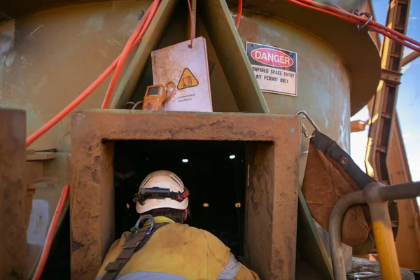 Safety workplace danger confined space sign defocused  certified trained worker wearing helmet PPE work uniform working as spotter stand by rescue at entry and exit confined space manhole gas test detector permit book 