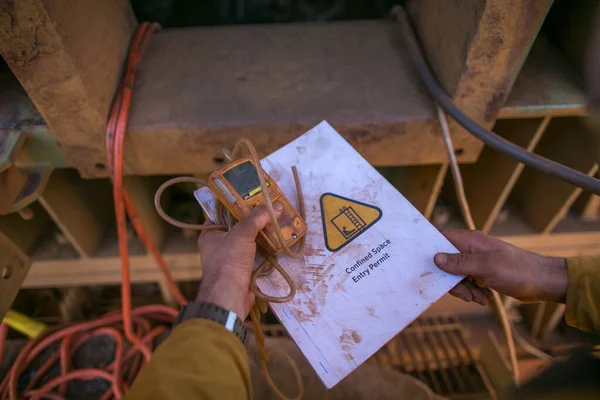 Safety work place certifies worker hands holding gas test detector atmosphere placing top of confined space permit book during pre starting work on site