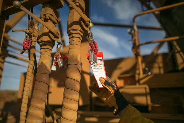 Isolation permit officer hand wearing a safety glove double checking danger isolation operation tag on the lock to make sure is placing on correct equipment construction mine site, Perth, Australia 
