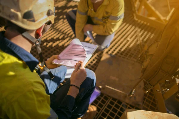 Safety work place construction miner wearing safety helmet hand over defocused of confined space working permit book to co-worker prior to starting early morning shift construction mine site Western Australian  