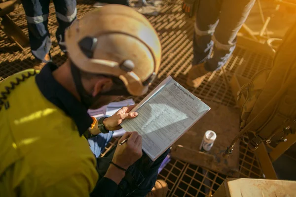Construction miner supervisor wearing white safety helmet signing working at height working permit on open field job site prior to starting high risk work each shift construction mine site Australia