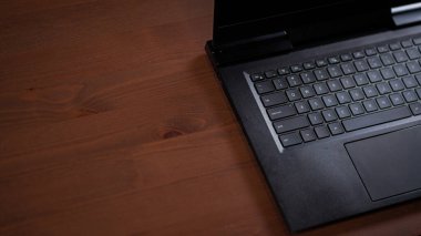 Black laptop keyboard and trackpad half in shot on wooden table background
