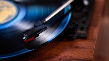 Vintage record with a blue hue playing on a turntable with a red needle on top of a brown wooden table