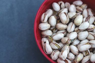 Kırmızı bir kasenin içinde siyah arka planda birkaç fıstık var.