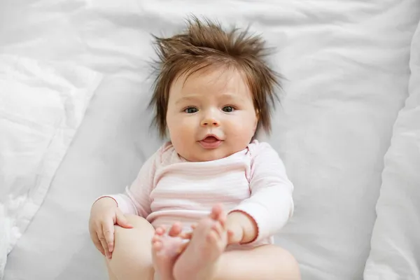 3 aylık bir bebek. Yeni doğmuş güzel bir kız bebek beyaz bir çarşafın üzerinde yatıyor. Bebek oynuyor ve gülümsüyor. Aile kavramı, annelik, bebek bakımı..