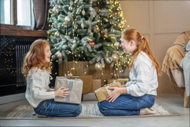 Rahat bir ev. Bej tonlarında modern iç mimari. Kazak ve kot pantolon giyen iki çocuk. Çocuklar gülümser.