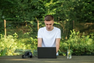 Dizüstü bilgisayarda çalışan bir adam, ahşap masadaki kır evinin bahçesinde gerçekten ilham verici bir yüze sahip.