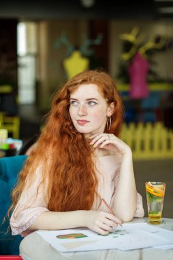 Yönetim ve pazarlama. Evrak işleri. Çok uzun kızıl saçlı. Öğrenci kafede materyal öğreniyor..