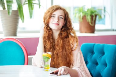 Nane, limon ve portakalla iç. Renkli tasarımı olan güzel bir kafede rahatlayın. Çilli surat. Güzel bir kadının portresi yalnız başına mocktail içiyor ve eğlenirken gülüyor..