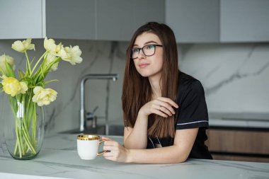 Gözlüklü esmer. Güzel siyah pijamalar. Sarı çiçekli güzel vazo. Samimi mutfak. Gri tonlarda modern iç mekan
