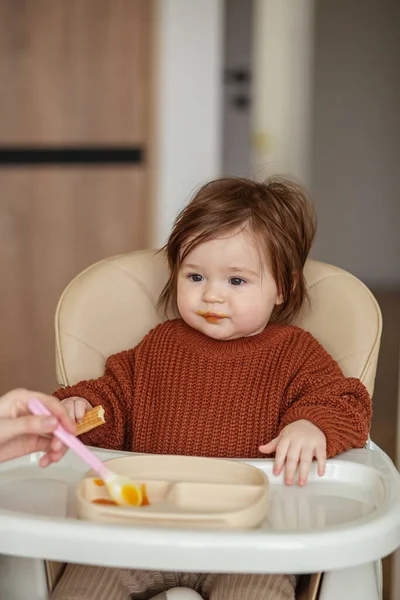 赤ちゃんのためのおいしいカボチャとリンゴのピューレ 茶色のセーターの幼児の女の子 ベビーシッターは小さな新生児を台所で養う — ストック写真