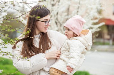 Mutlu kadın ve küçük çocuk baharda çiçek bahçesinde yürüyor ve sarılıyorlar. Mutlu bir aile. Anneler günü tatili konsepti.