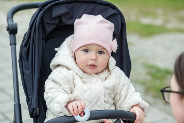 Küçük çok güzel kız şık bir siyah bebek arabasında oturuyor. Nazikçe pembe şapka ve bej ceket. Bahar ve yaz mevsimi.