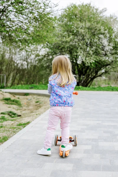 小さな幼児の女の子は春の日にシティパークでキックスクーターに乗ることを学びます かわいい未就学児が屋外で遊んでいる 子供のためのアクティブなレクリエーションや屋外スポーツ — ストック写真