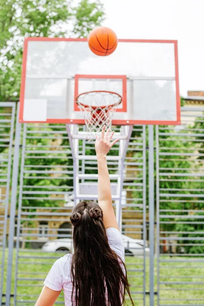 Concept of sports, hobbies and healthy lifestyle. Young athletic woman is training to play basketball on modern outdoor basketball court.