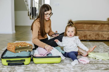 Tatil hazırlığı. Genç kadın bebekle yolculuk için bavulunu hazırlıyor..