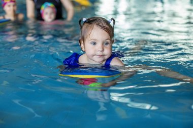 Small preschooler child learns to swim with board in pool. Swimming lesson. Active child plays in water.