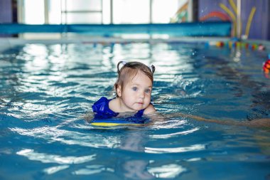 Small preschooler child learns to swim with board in pool. Swimming lesson. Active child plays in water.