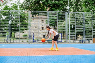 Spor anlayışı, hobiler ve sağlıklı yaşam tarzı. Genç atletik kadın, modern açık hava basketbol sahasında basketbol oynamak için antrenman yapıyor..