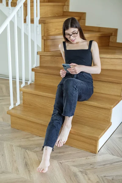 Young woman on stairs at home relaxing, reading email using mobile device and mobile wifi.
