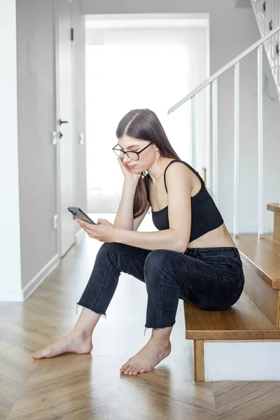 Young woman on stairs at home relaxing, reading email using mobile device and mobile wifi.