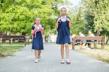 İki mutlu çocuk sırt çantalarıyla okula gider. Okula, öğrenmeye, arkadaşlığa ve çocukluğa geri dön..