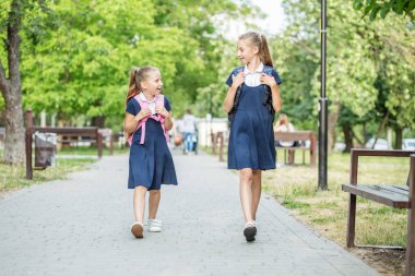 İki mutlu çocuk sırt çantalarıyla okula gider. Okula, öğrenmeye, arkadaşlığa ve çocukluğa geri dön..
