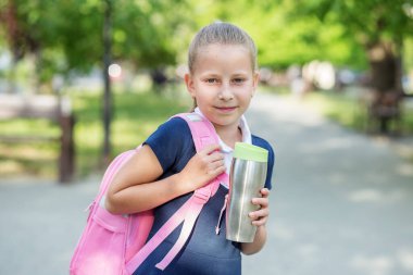 Gülümseyen liseli kız okula pembe sırt çantası ve metal termo bardakla gidiyor. Okula, eğitime ve çocukluğa dönüş kavramı.
