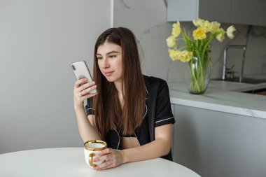 Gülümseyen kadın telefon mesajını okuyor. Esmer, mutlu kız mesaj yazıyor. Vazoda sarı laleler..