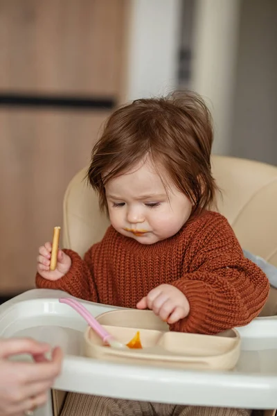 Delicious pumpkin and apple puree for babies. Toddler girl in brown sweater. Vertical.