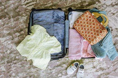 Children's travel suitcase with clothes and shoes on floor of room. Vacation with children concept. Top view