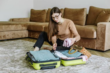 Seyahat modası. Tatil plajı. Plaj çantası. Mutlu genç bir kadın evdeki seyahat bavulunu hazırlıyor. Tatil hazırlığı. Turist gezisi.