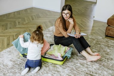 Tatil hazırlığı. Genç kadın bebekle yolculuk için bavulunu hazırlıyor. Gerekli şeylerin defterinde listele.