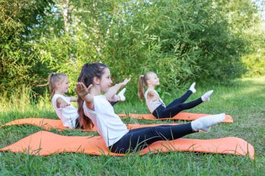 Group of children are doing exercises and stretching in nature using sports mats. Workout with gymnastics or aerobics or dance. Healthy lifestyle