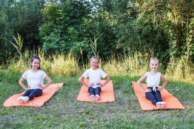 Group of children are doing exercises and stretching in nature using sports mats. Workout with gymnastics or aerobics or dance. Healthy lifestyle