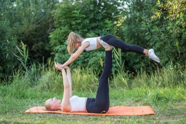 Mother lies on back and keeps daughter on feet during fitness in park. Concept of sports, healthy lifestyle and hobbies