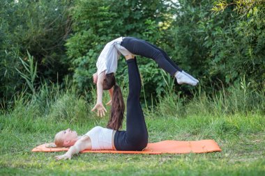 Mother lies on back and keeps daughter on feet during fitness in park. Concept of sports, healthy lifestyle and hobbies