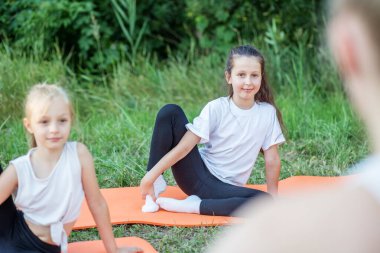 Group of children are doing exercises and stretching in nature using sports mats. Workout with gymnastics or aerobics or dance. Healthy lifestyle