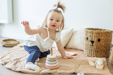 Toddler child plays with developmental toys. Little girl makes pyramid. Basket for toys. Cozy home. Happy baby