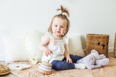 Toddler child plays with developmental toys. Little girl makes pyramid. Basket for toys. Cozy home. Happy baby