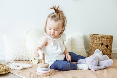 Toddler child plays with developmental toys. Little girl makes pyramid. Basket for toys. Cozy home. Happy baby