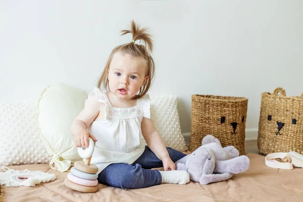 Toddler child plays with developmental toys. Little girl makes pyramid. Basket for toys. Cozy home. Happy baby