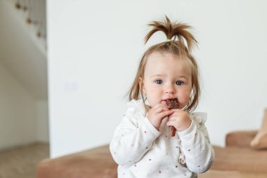 Little baby toddler eats sweet healthy fruit paste rolls. Fruit-flavored snack rolled into tube. Concept of childhood, healthy food and lifestyle.