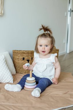 Toddler child plays with developmental toys. Little girl makes pyramid. Basket for toys. Cozy home. Happy baby