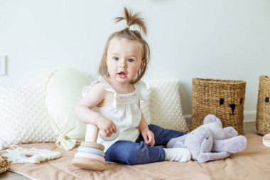 Toddler child plays with developmental toys. Little girl makes pyramid. Basket for toys. Cozy home. Happy baby