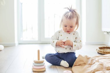 Toddler child plays with developmental toys. Little girl makes pyramid. Basket for toys. Cozy home. Happy baby
