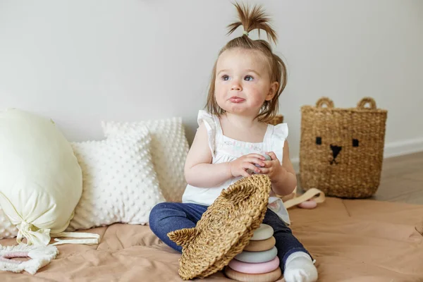 Toddler child plays with developmental toys. Little girl makes pyramid. Basket for toys. Cozy home. Happy baby