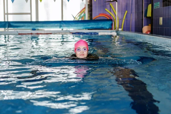 Woman swims in swimming pool. Goggles and swimming cap. Concept of sports, exercise and healthy lifestyle